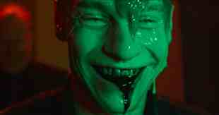 A man coated in green slime vomits up black sludge.