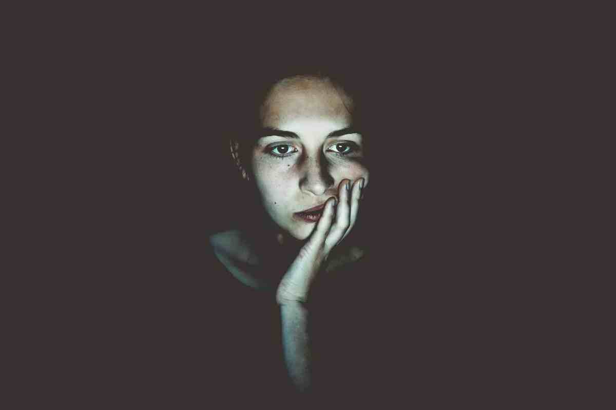 A woman sits in darkness, her face illuminated by a screen, looking a little fatigued.