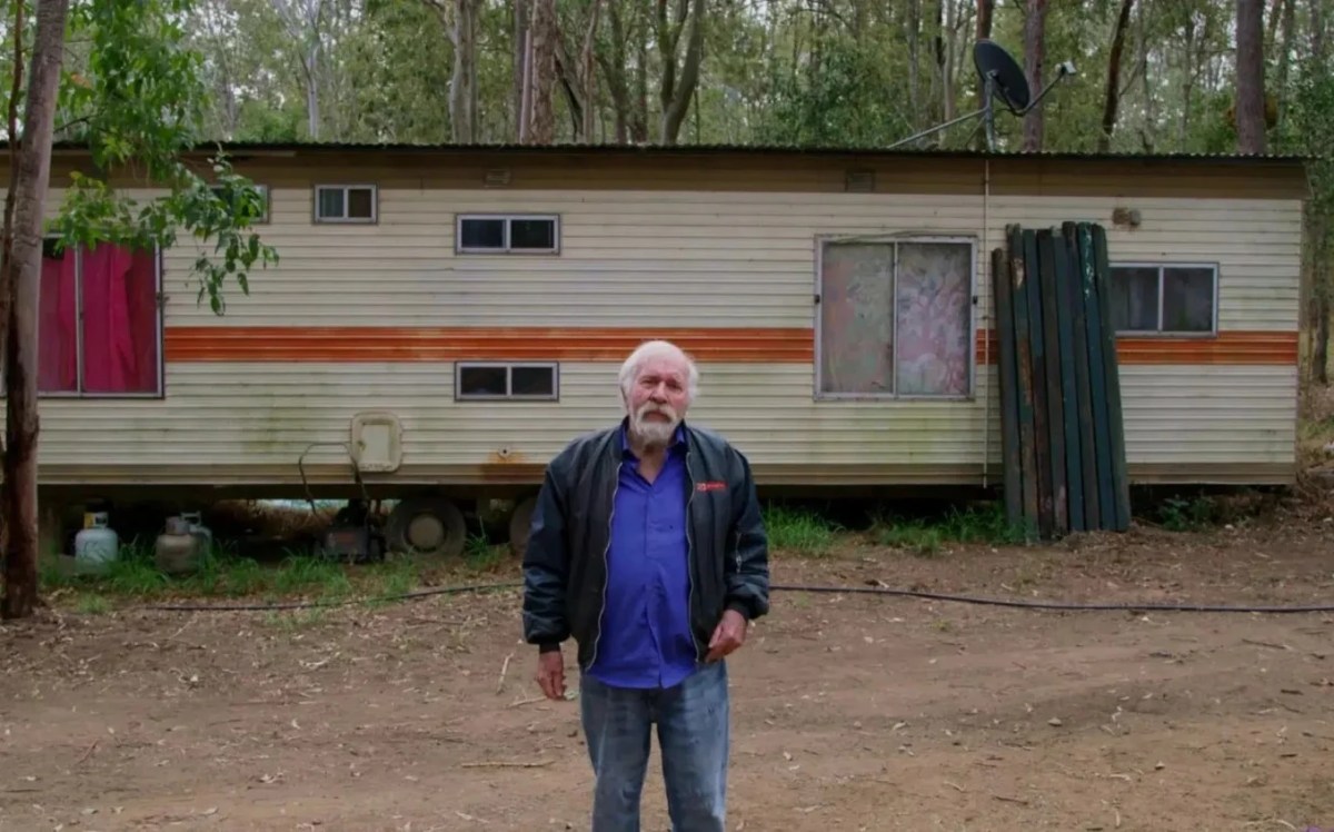 A documentary on Jack Karlson titled ‘ The Man Who Ate A Succulent Chinese Meal’. Image: Kicking Television Productions. An old Caucasian man with grey hair and beard stand outside a caravan house in the woods.