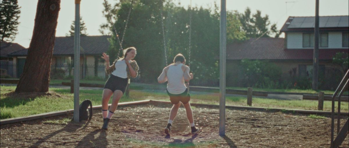 Developing a broad skillset. Two teenagers sit on park swings in a suburban landscape. One sits with his back to the camera, the other has twisted their swing around to talk to him.