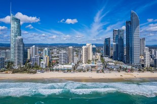 Aerial front view Surfers Paradise foreshore high-rise buildings from above Pacific Ocean; breaking waves in foreground, low-rise suburbs and hinterland hills on the distant horizon:higher elevation. Sunny day with some clouds.